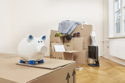 A piggy bank sits on a packed box in a packed living room - Cal Home Real Estate Services